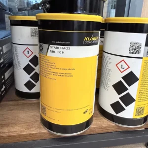 Industrial lubricant can from Kluber Lubrication with yellow label and hazard symbol, displayed on a wooden shelf