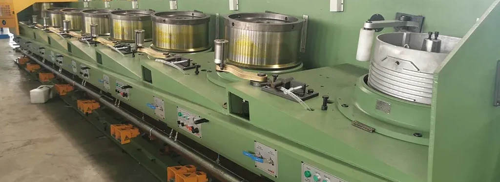 Green manufacturing machine with several large reel spools on top and control panels along the side in a factory setting.